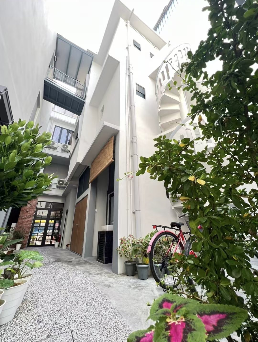 White courtyard with plants, spiral staircase and a red bicycle